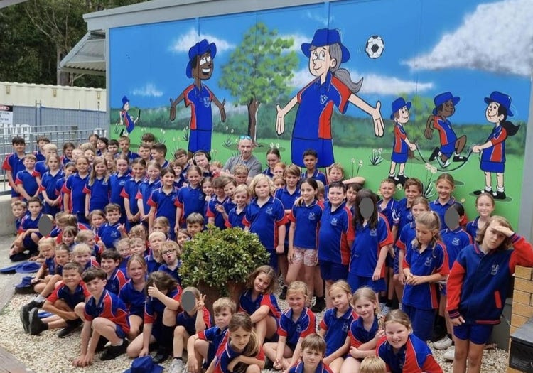 All of Bonville students in front of the new mural they helped paint. The mural shows cartoon style pictures of kids in Bonville uniform, playing in the playground.