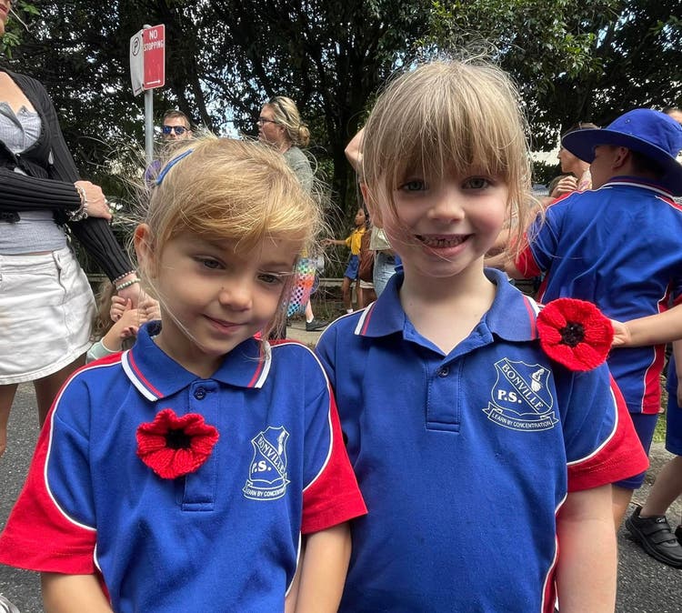 Two young students in school uniform with red poppies on their shirts at the Anzac day march.