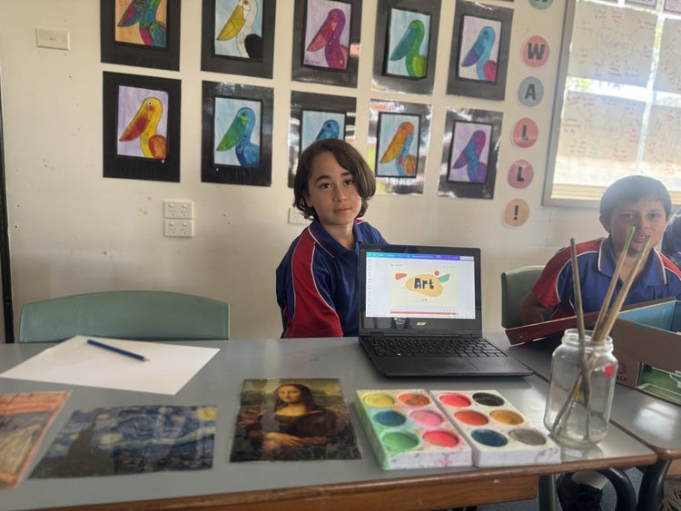 A year five student displaying his research project on his laptop alongside art materials