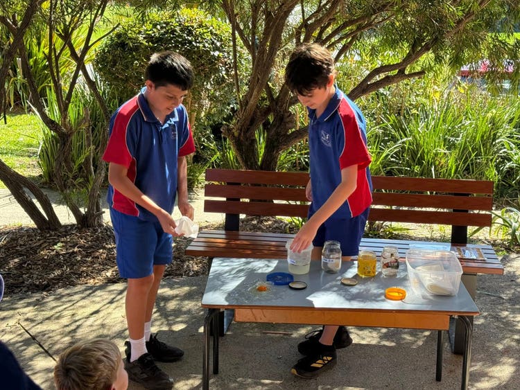Two year five students demonstrating a science experiment on a table in an outdoor learning area