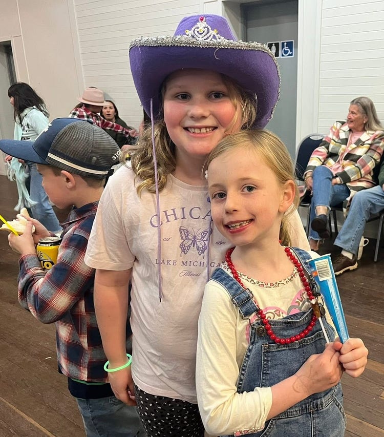 Two smiling girls at the school bush dance in the hall. One is wearing a cowgirl style hat.
