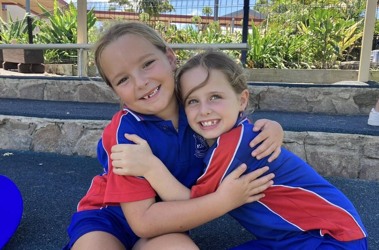 Two year three girls hugging each other while smiling at the camera