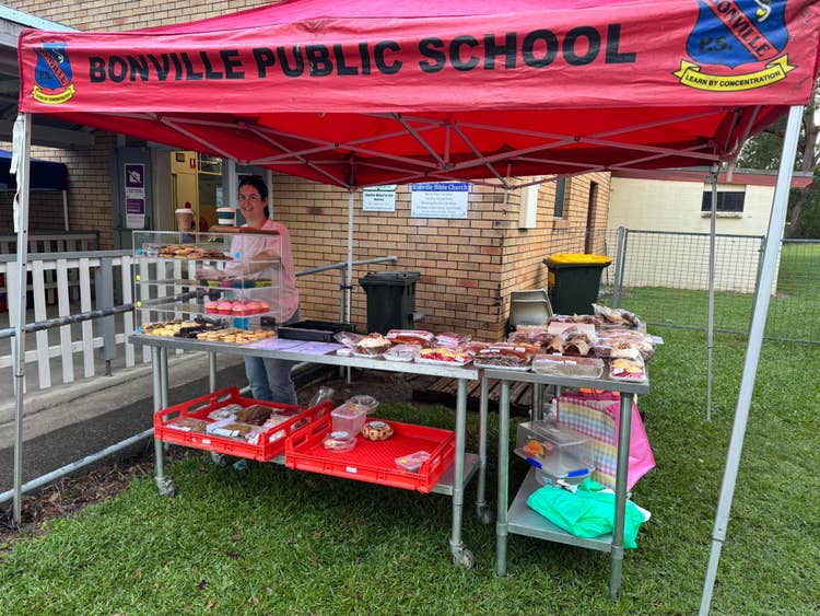 A parent volunteer standing in front of a cake stall, underneath the Bonville Public School gazebo on election day.